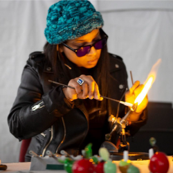 A headshot of an artist wearing a beanie and blowing glass